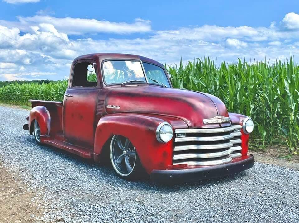 Red patina Chevrolet pickup beside a cornfield